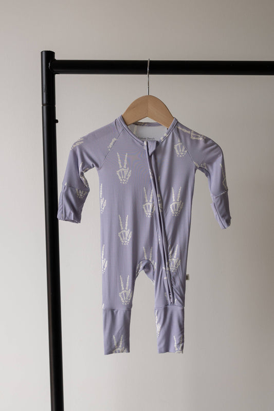 Forever French Baby Enchanted Skelly bamboo zip pajamas on a hanger, lavender with a white skeleton print