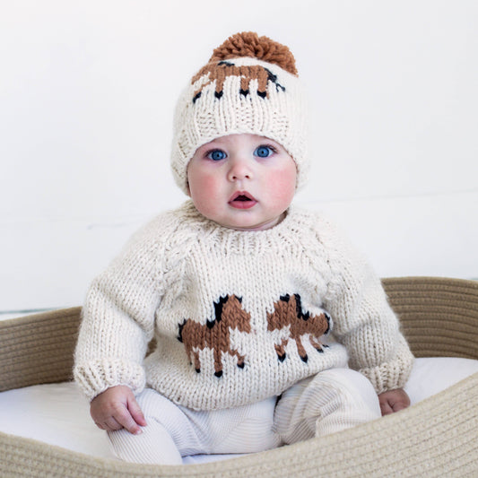 Baby wearing a knitted sweater with horse patterns and a matching hat.