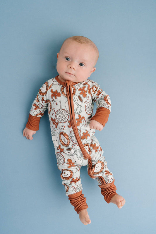 Baby wearing our hot cocoa bamboo sleeper with 2 way zipper. These hot cocoa pajamas feature gingerbread man cookies, hot chocolate, snowman and more Christmas cheer! Buttery soft, lightweight, breathable, and stretchy. Fold over mittens up to 12-18M. Fold over footies.