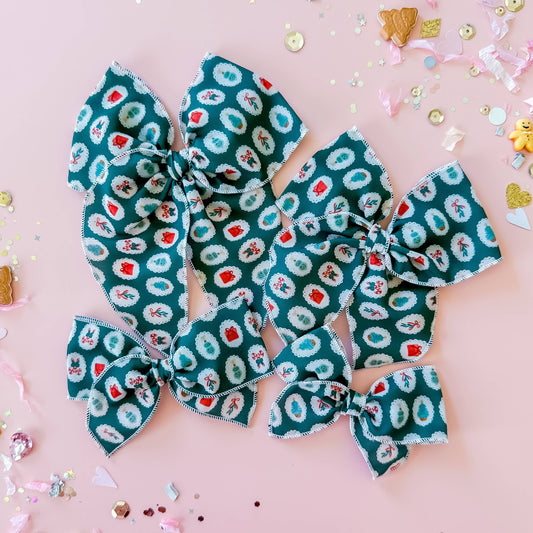 Two large green patterned hair bows on a pink background with confetti.
