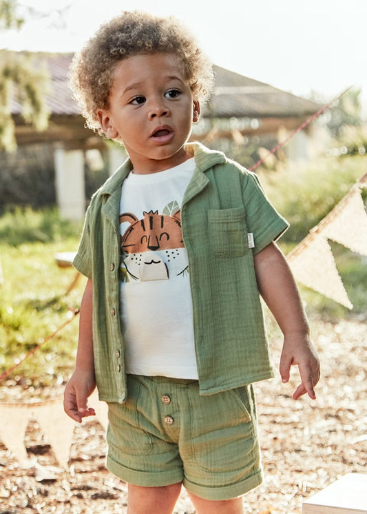Child wearing a green outfit with a shirt featuring a fox design, standing outdoors.