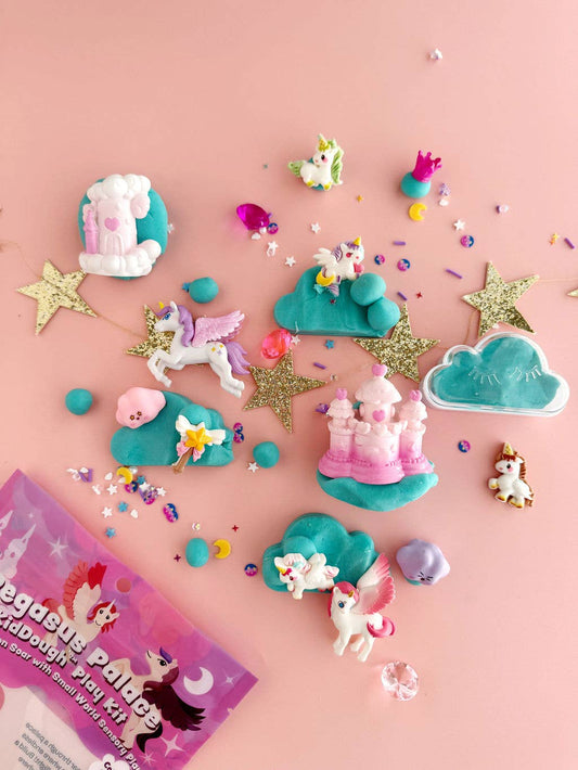Pastel pink and blue Pegasus Palace KidDough with unicorn figures, stars and sprinkles spread beside the pouch on pink