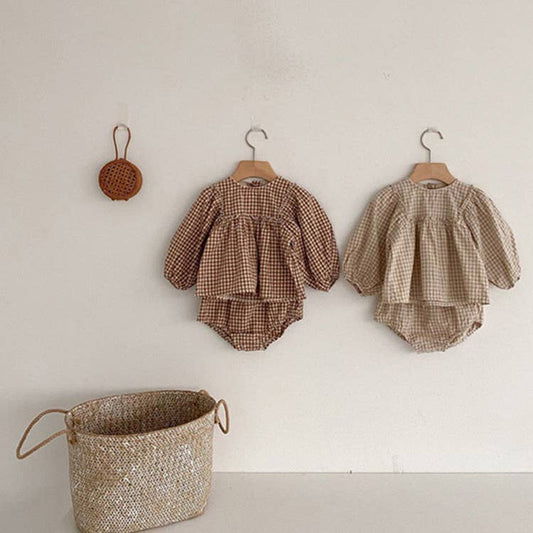Brown gingham puff sleeve romper and bloomer set hanging on wall pegs above a woven basket