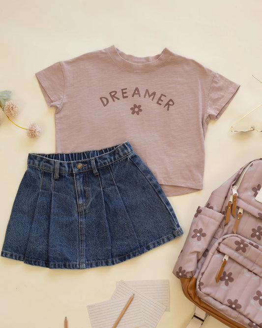 Styling flat lay of the Rylee + Cru Dreamer boxy tee with a pleated denim skirt and a floral backpack