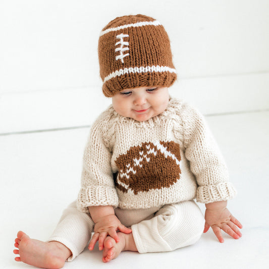 Baby lying down wearing the Huggalugs knit football beanie and a cream sweater