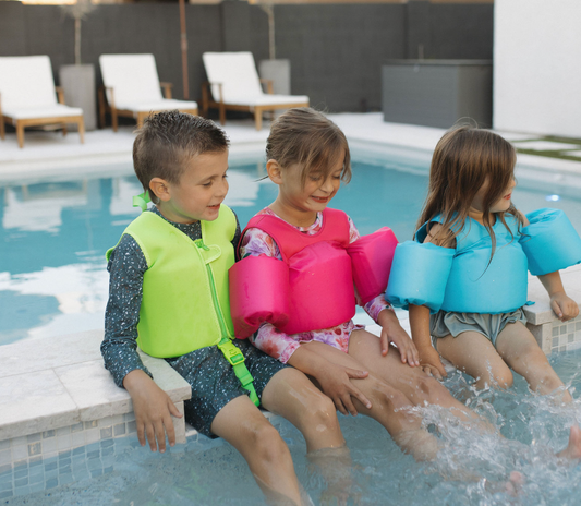 Kids sitting on the side of a pool wearing The "Brights" High Visibility Neon Swim Floaties