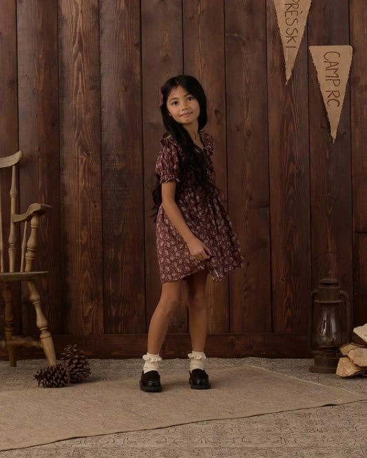 girl wearing a fall dress standing in front of a wooden wall 
