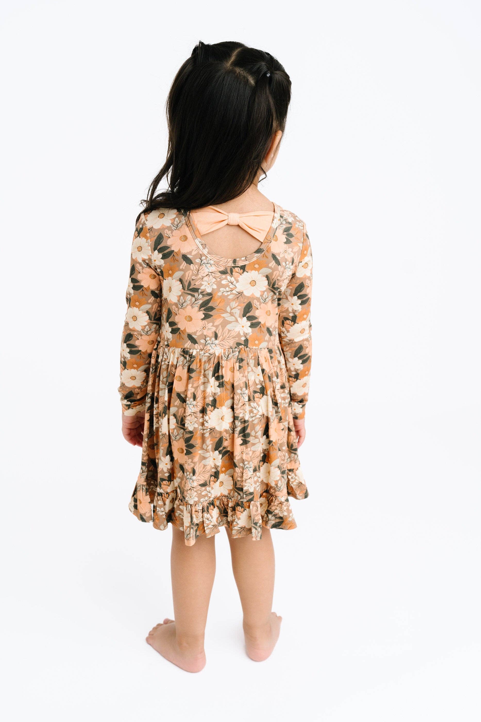 Young girl wearing a floral dress with bow detail on back on a white background