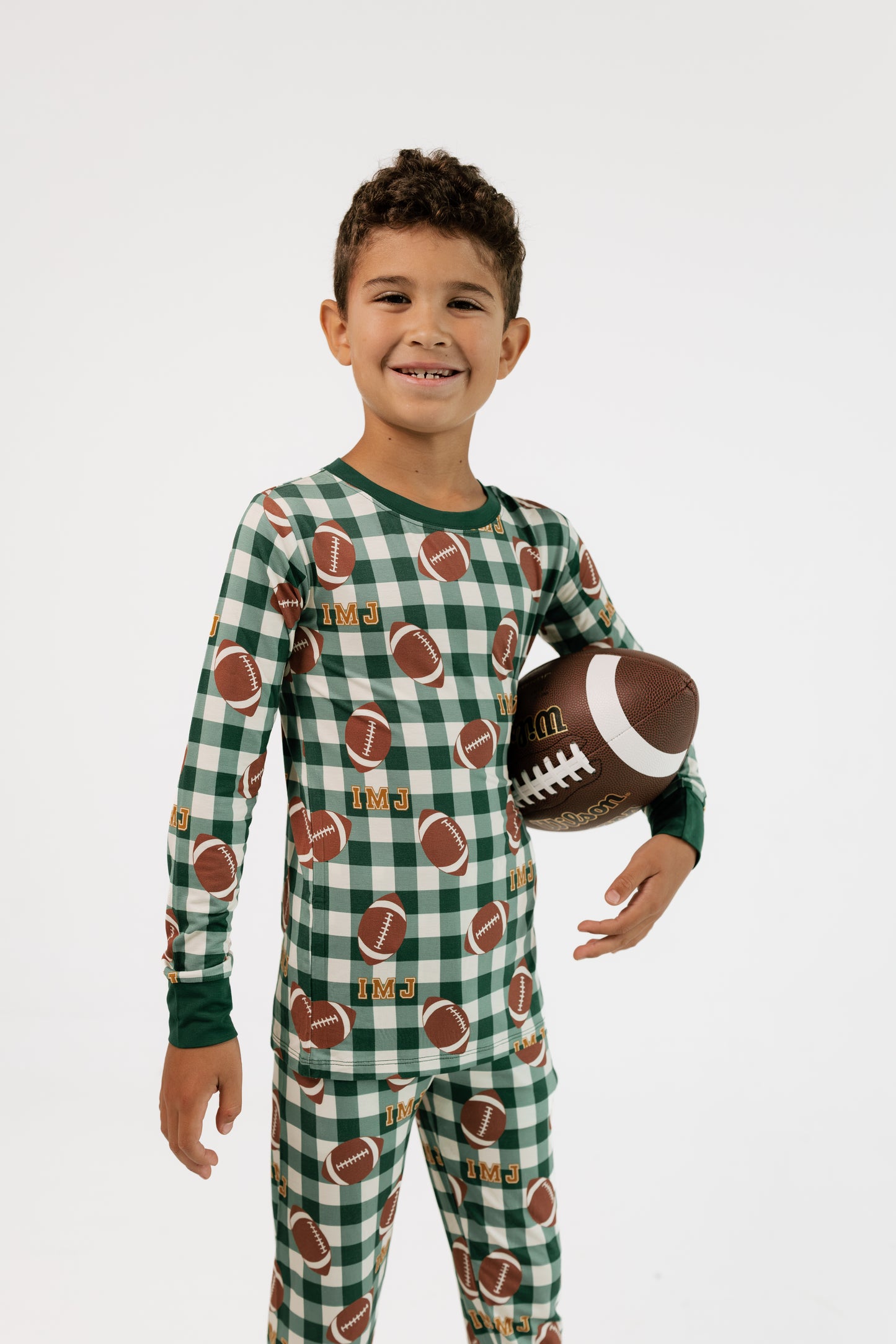 Boy wearing In My Jammers Game Day Gingham two piece bamboo pajama set in green plaid, holding a football