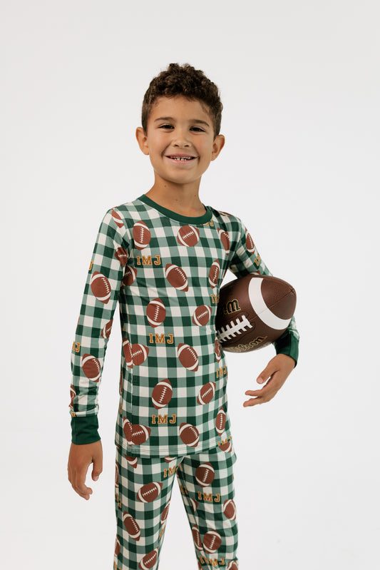 Boy wearing In My Jammers Game Day Gingham two piece bamboo pajama set in green plaid, holding a football