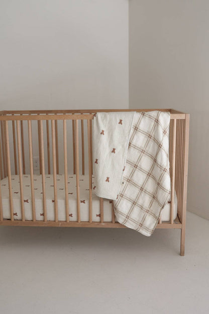 Teddy and Ellis Plaid muslin baby quilt folded over the side of a crib in a neutral nursery