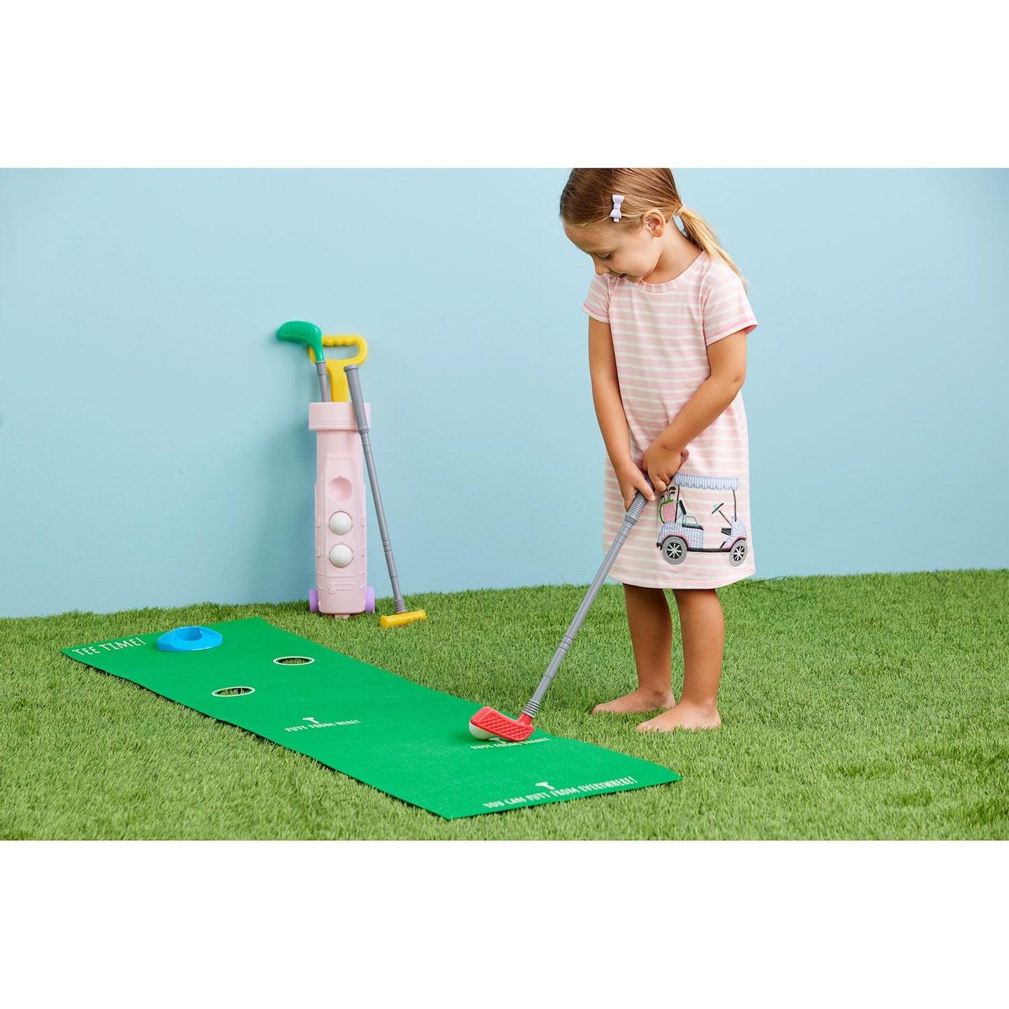 Girl playing golf with her 9-piece Pink golf set. Plastic golf bag holds three clubs, three balls, one hole and flag and one felt putting green. Ages 3+