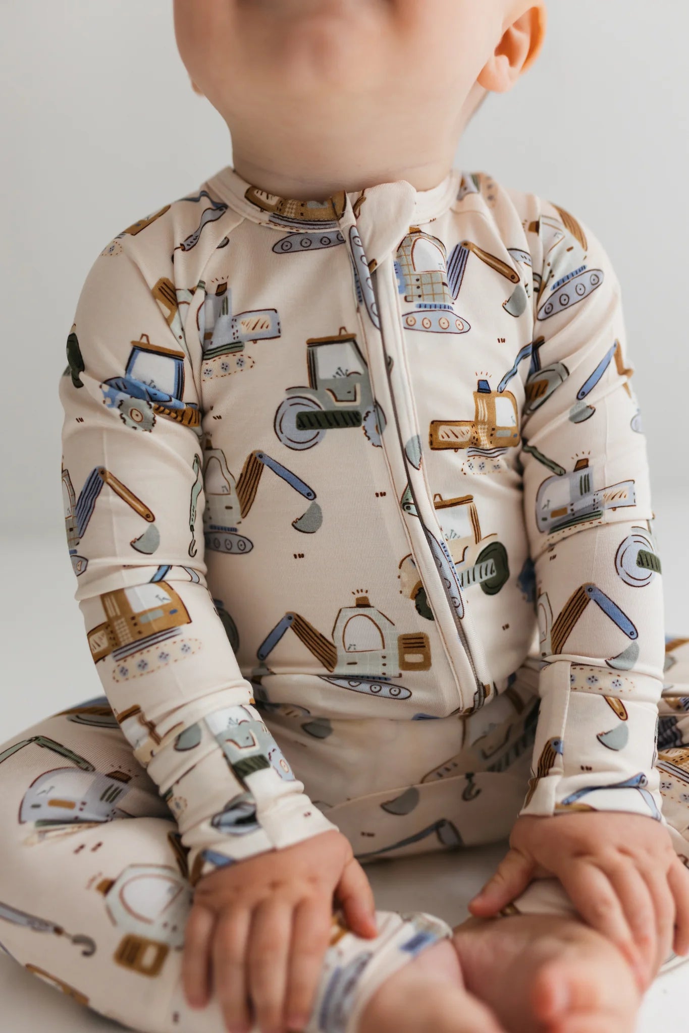 Child wearing a patterned onesie with construction vehicles on a plain background