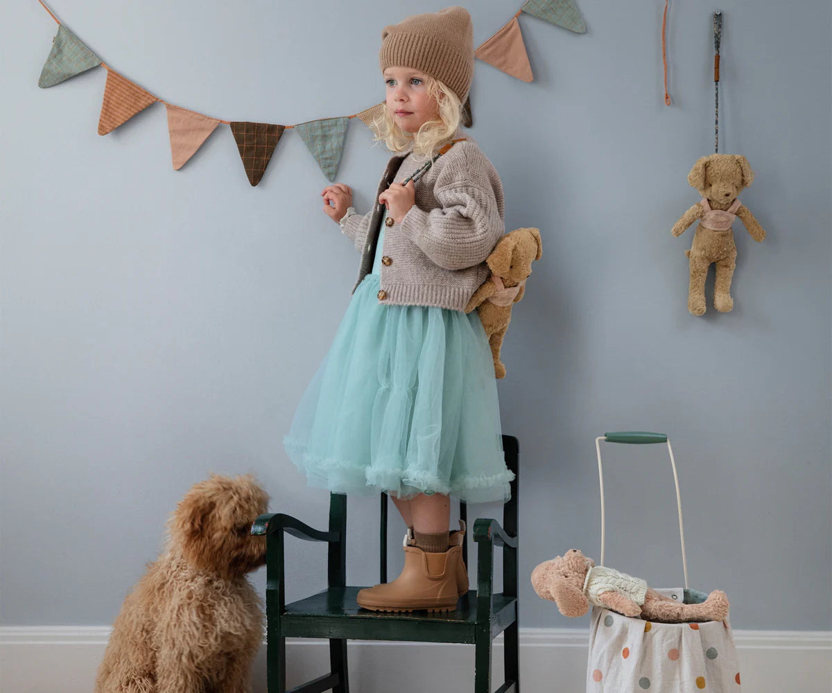 Girl standing on chair surrounded by her goldendoodle puppy and her Maileg puppies wearing the Puppy Supply harness. 