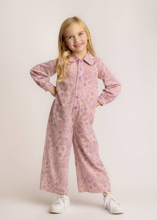 Young girl wearing a pink floral jumpsuit on a light background