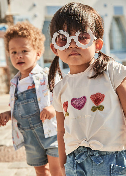 Girl wearing Toddler Girls T-Shirt with Floral Crochet Appliqué. Boy in background wearing overalls and surf shirt. 