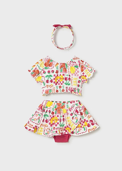 Children's outfit set with top, skirt, and headband featuring a colorful fruit pattern on a light gray background.