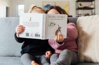 Two children sitting on a couch reading a book titled 'Scribble Scrabble'.