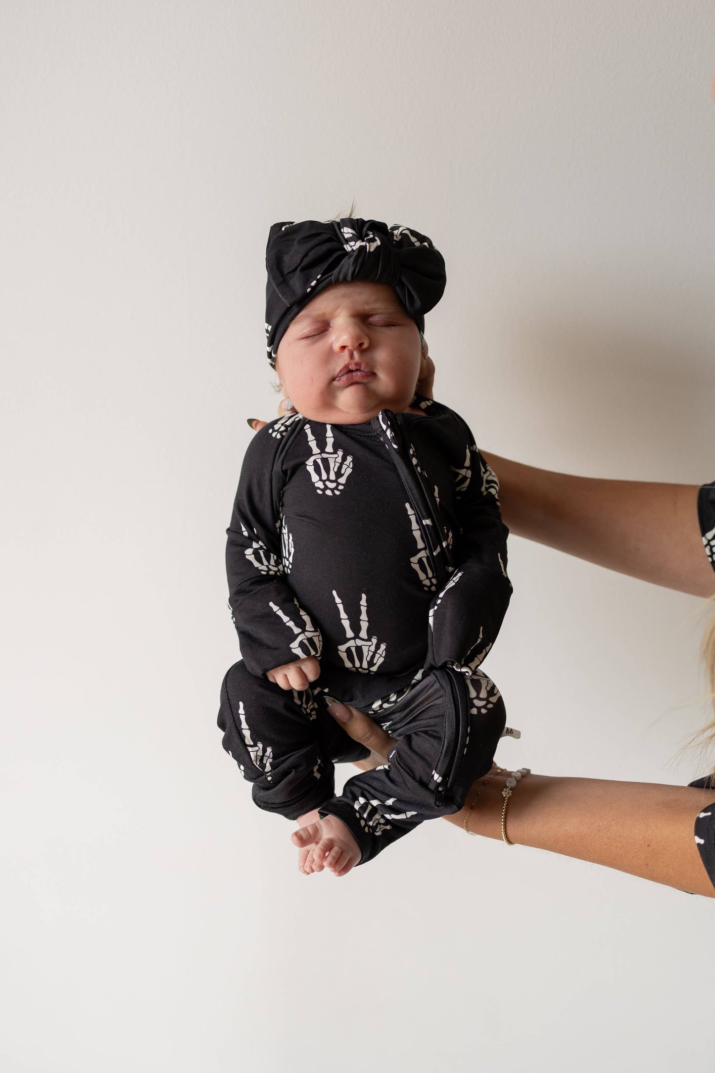 Baby held up in black Midnight Skelly bamboo zip pajamas with a matching knotted hat