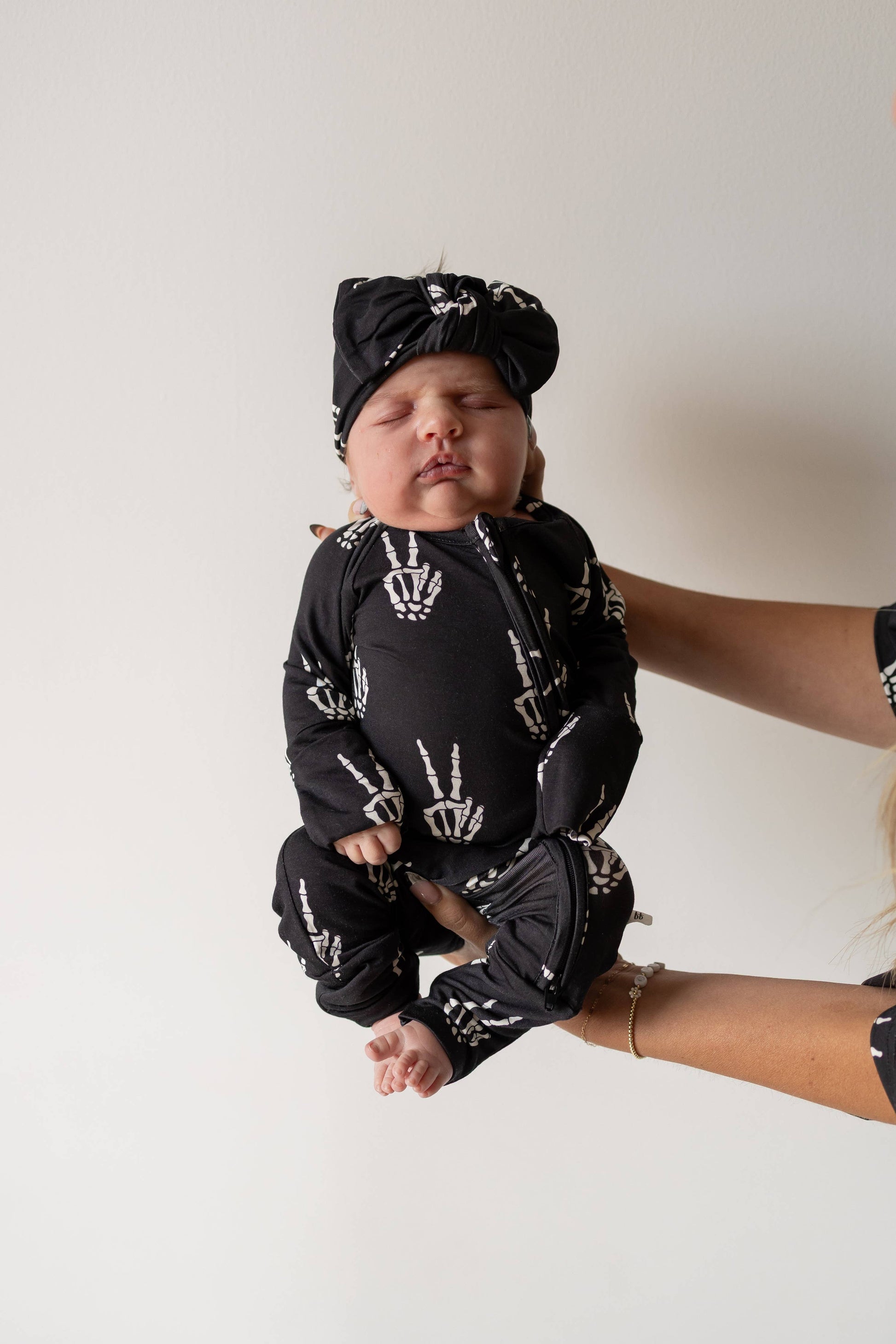 Baby held up in black Midnight Skelly bamboo zip pajamas with a matching knotted hat