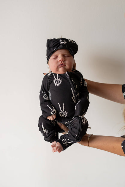 Baby held up in black Midnight Skelly bamboo zip pajamas with a matching knotted hat