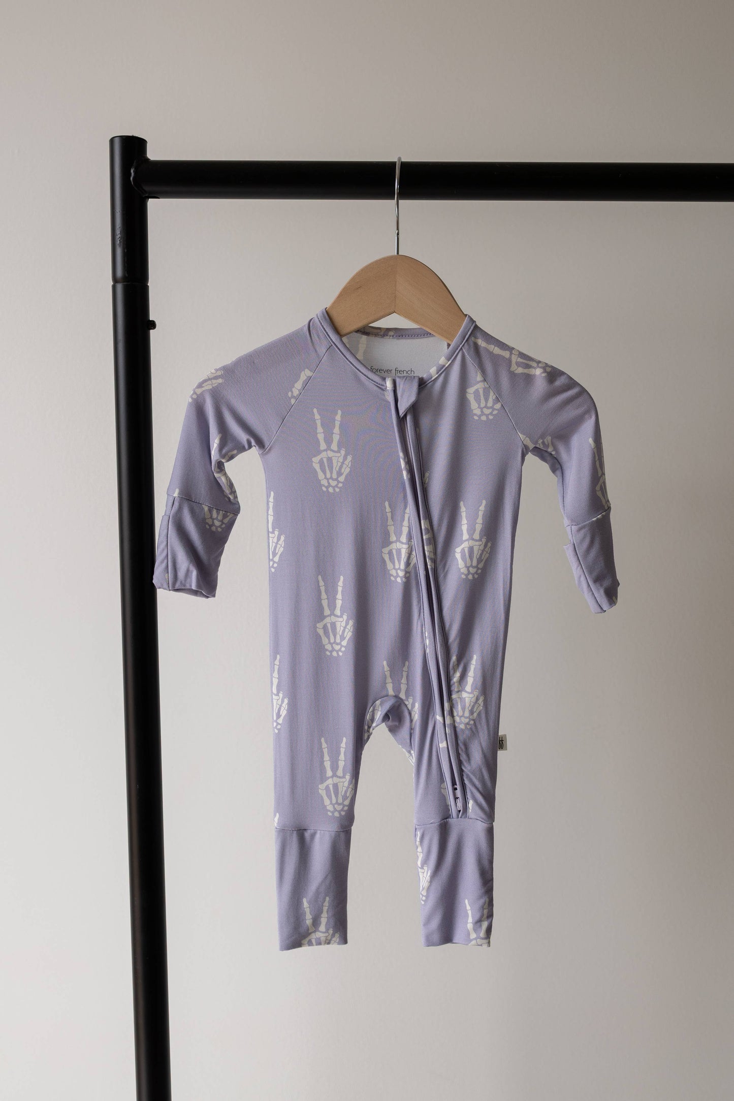 Forever French Baby Enchanted Skelly bamboo zip pajamas on a hanger, lavender with a white skeleton print