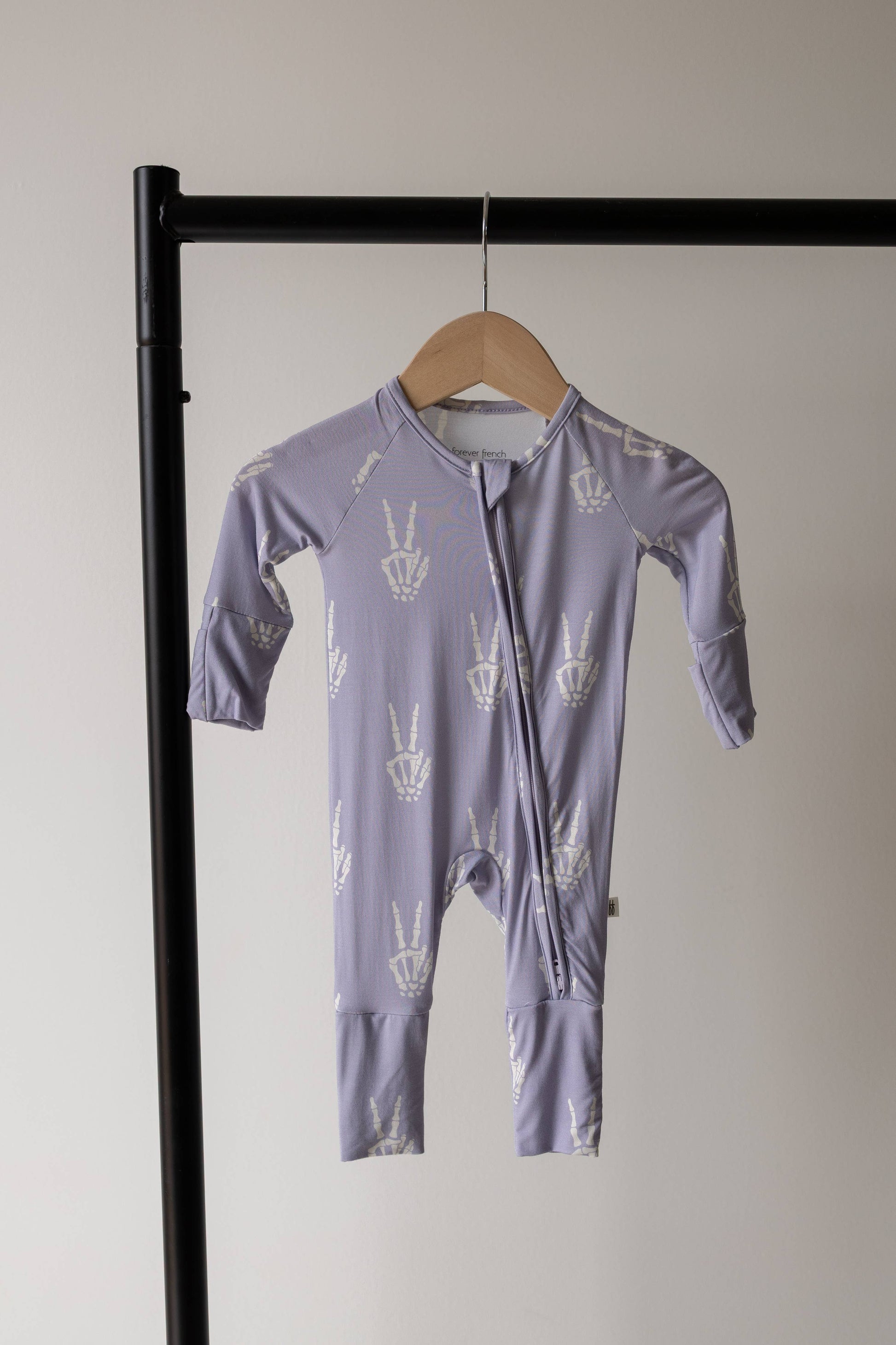 Forever French Baby Enchanted Skelly bamboo zip pajamas on a hanger, lavender with a white skeleton print