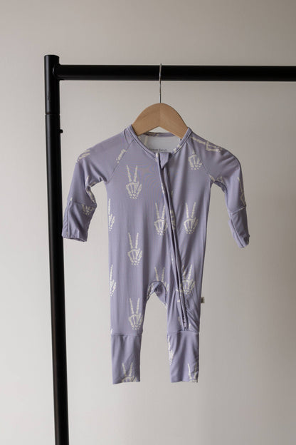 Forever French Baby Enchanted Skelly bamboo zip pajamas on a hanger, lavender with a white skeleton print