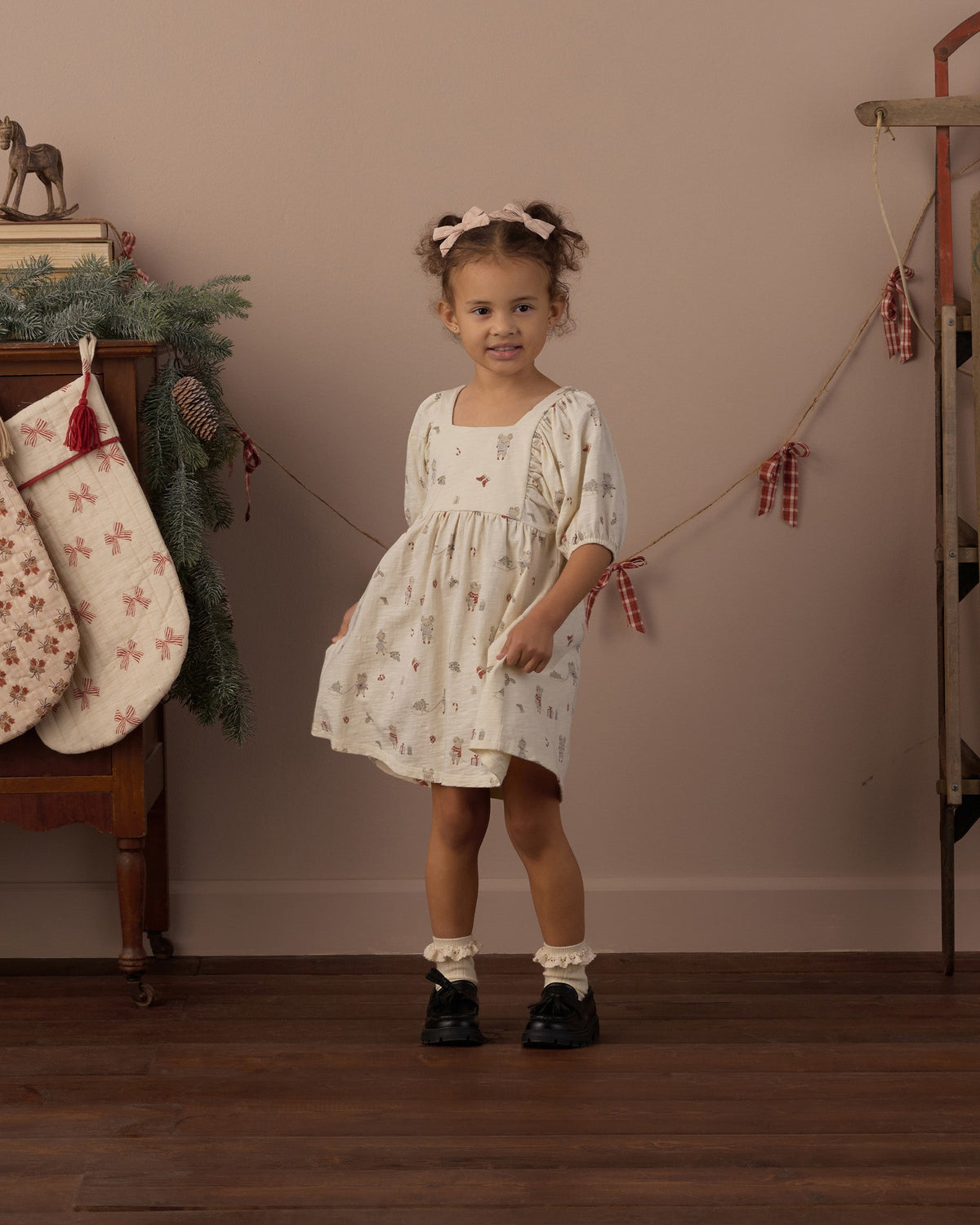 Girl with pigtails wearing the Rylee + Cru Brea dress in holiday mouse print beside a Christmas stocking and garland