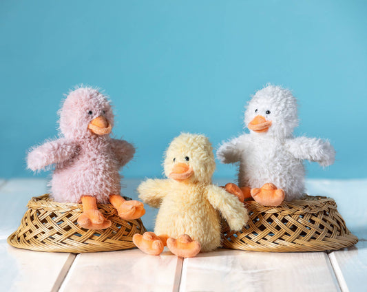 Three fluffy toy ducks on a white surface with a blue background