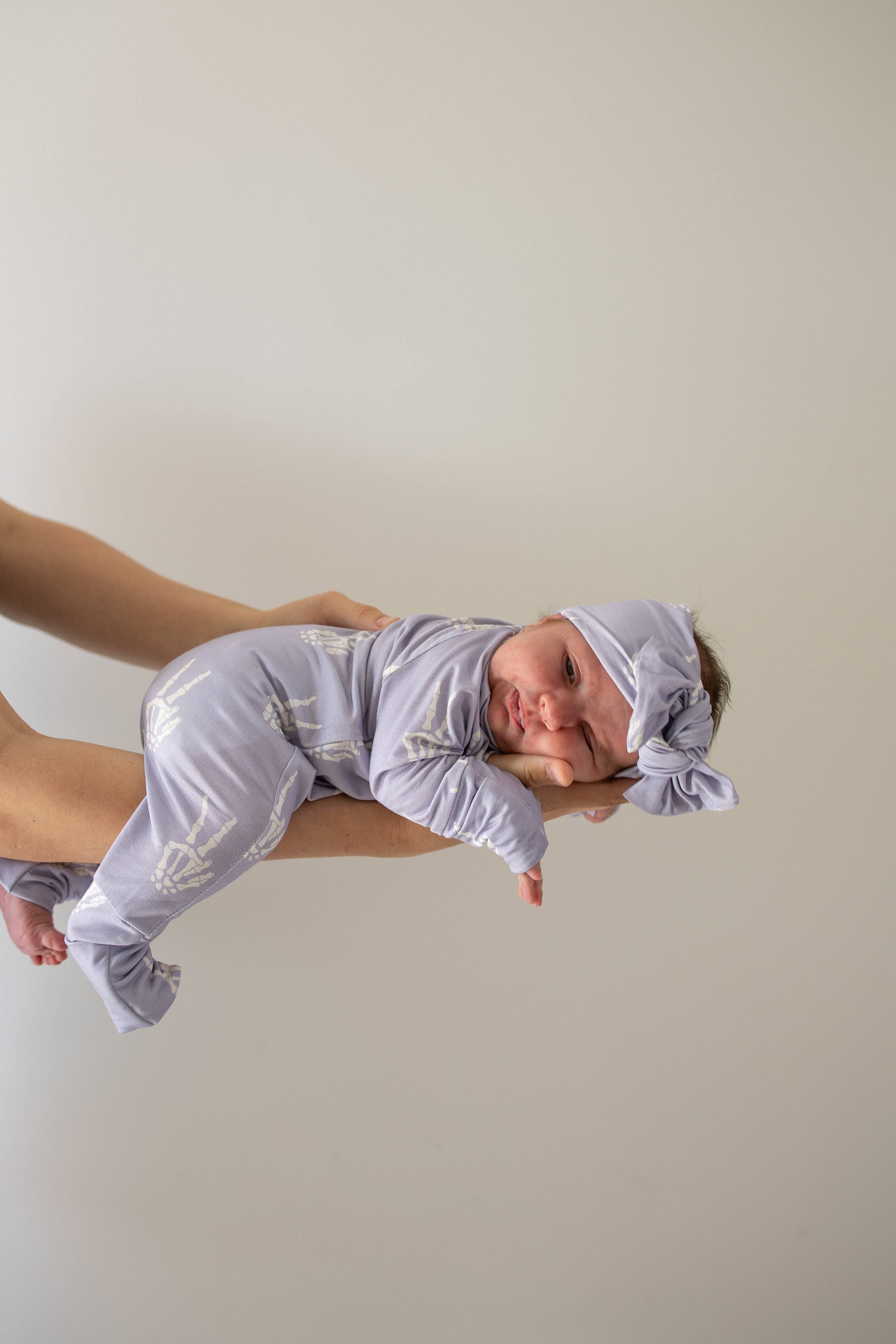 Baby held up wearing the Enchanted Skelly bamboo head wrap and matching lavender skeleton print pajamas