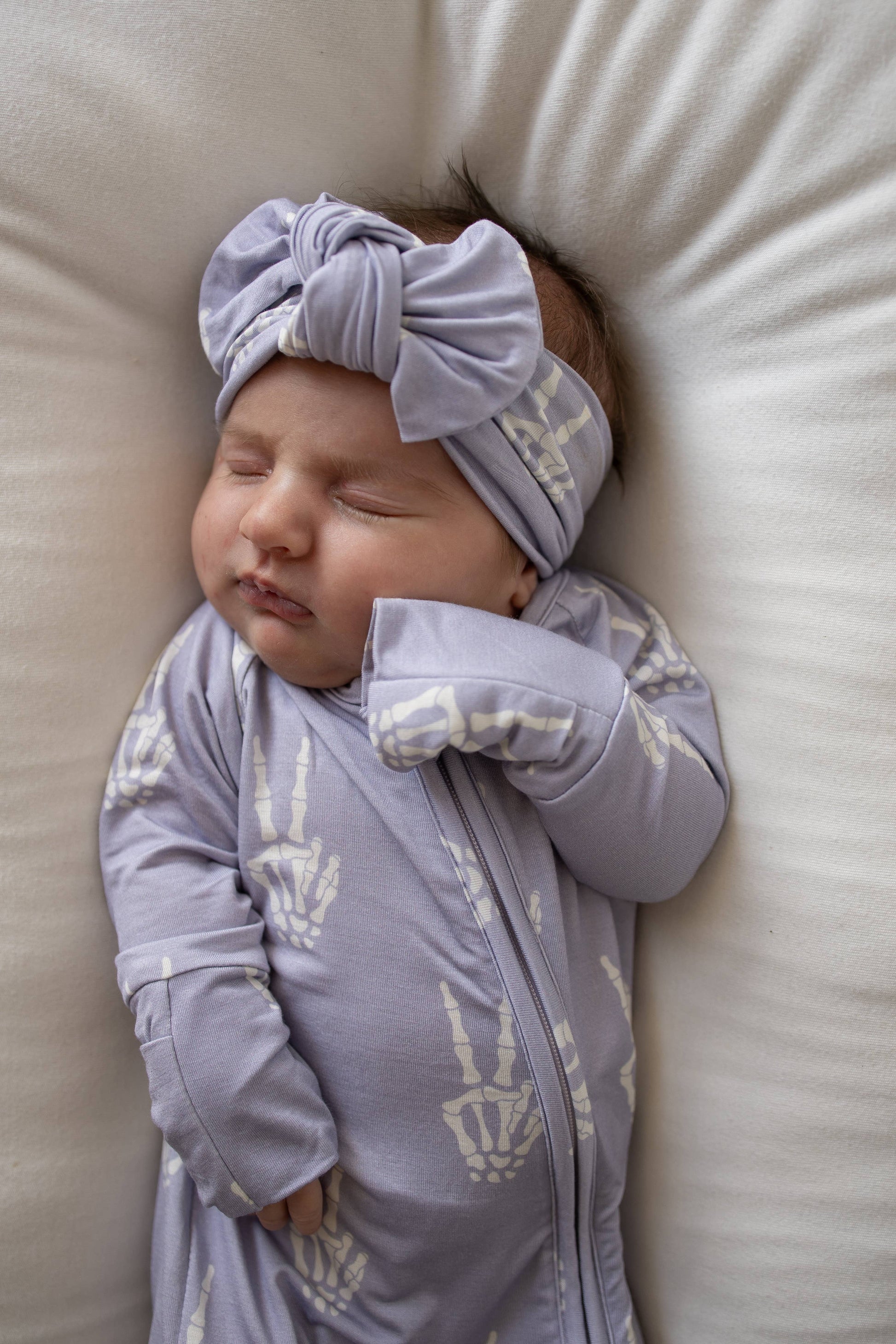 Sleeping baby wearing the lavender Enchanted Skelly head wrap and matching bamboo pajamas