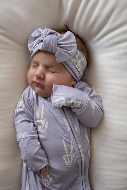 Sleeping baby wearing the lavender Enchanted Skelly head wrap and matching bamboo pajamas