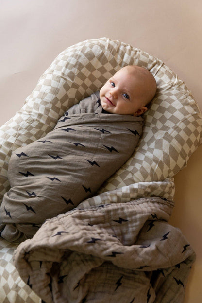 Baby wrapped in the reversible lightning bolt and wavy checkerboard muslin quilt in a lounger