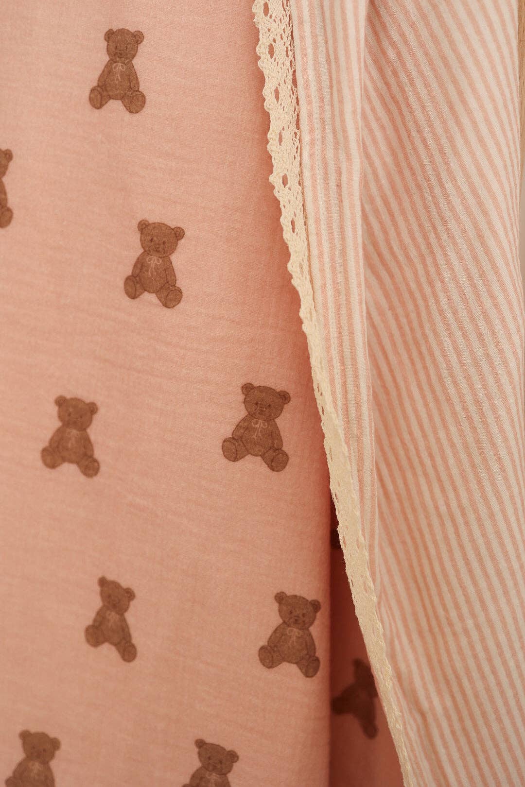 Close-up of a pink fabric with teddy bear pattern and a striped fabric edge.