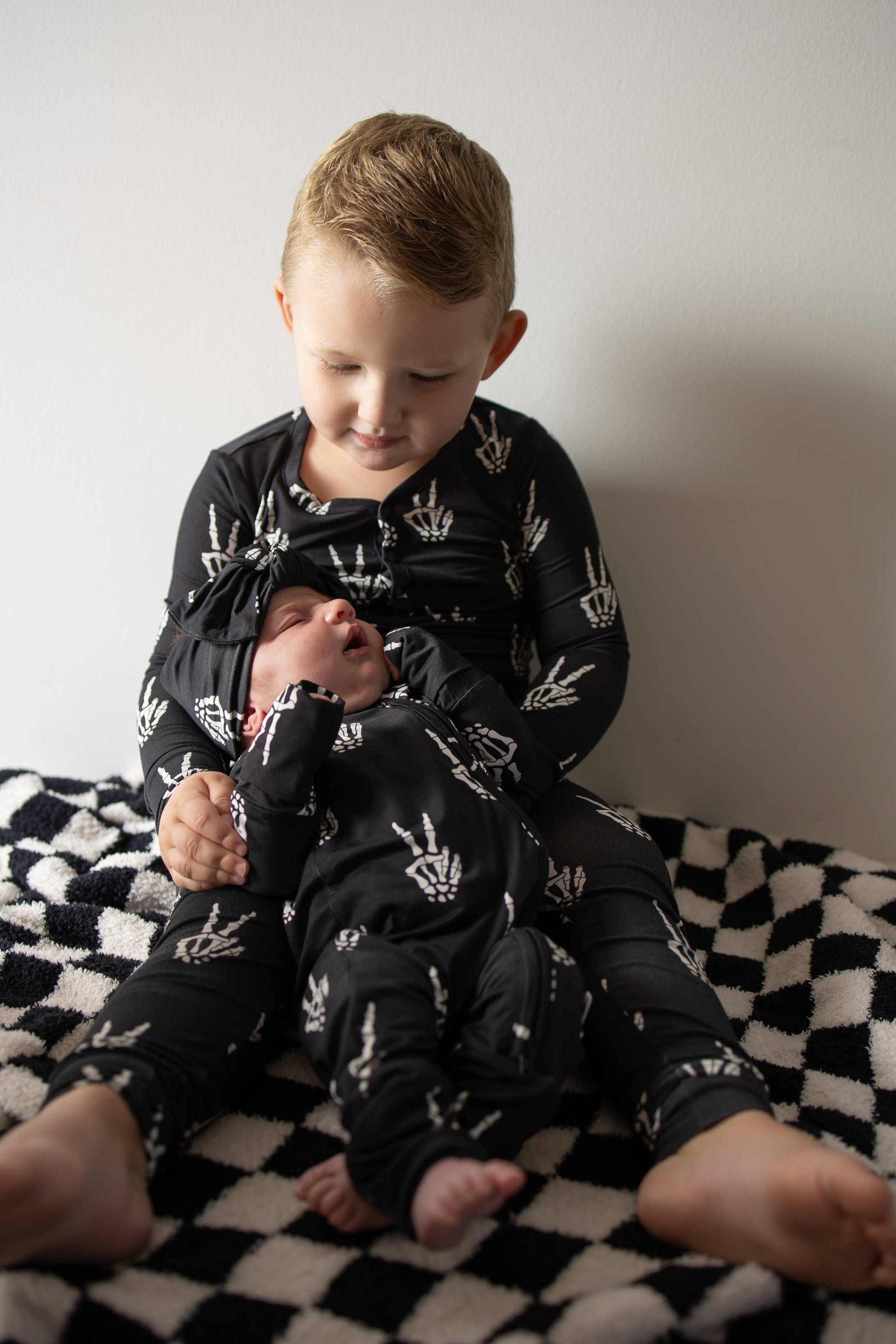 Toddler sitting on a checkered blanket in black Midnight Skelly bamboo zip pajamas