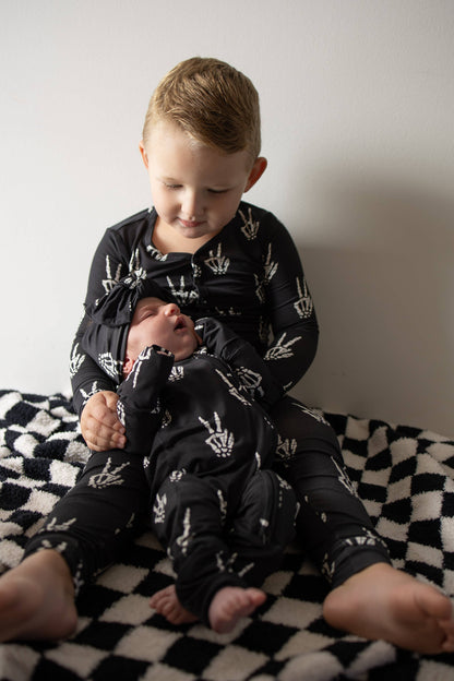 Toddler sitting on a checkered blanket in black Midnight Skelly bamboo zip pajamas