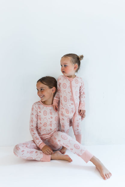 Two children wearing matching pink ballet slipper pajamas with a white background
