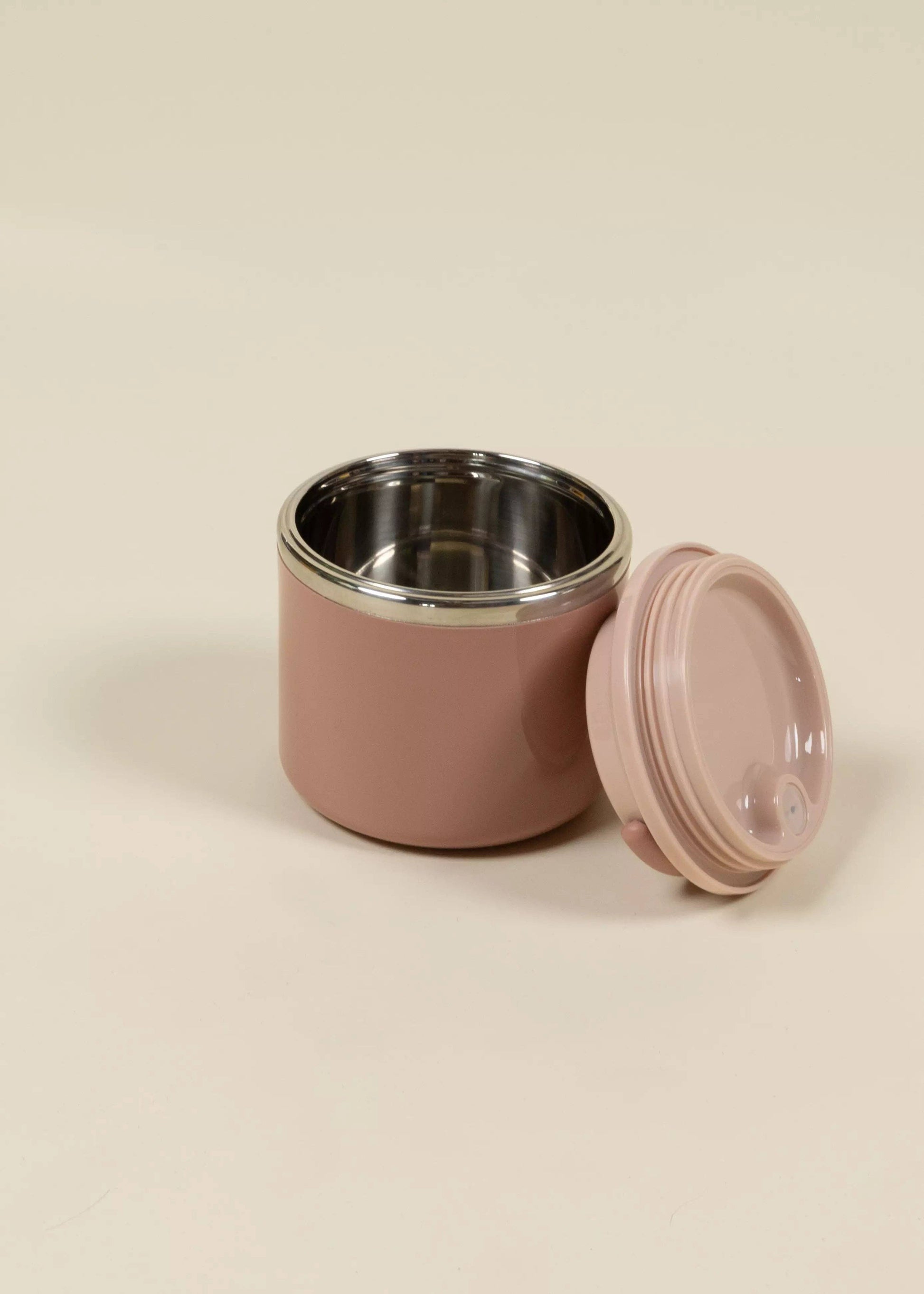 Pink food container with a silver interior and pink lid on a beige background