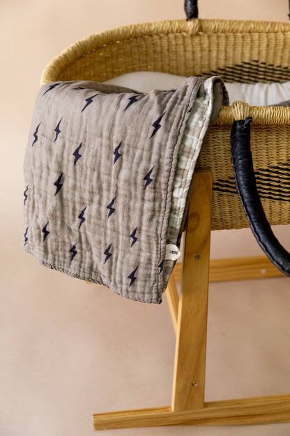 Lightning bolt and wavy checker muslin baby quilt hanging over a moses basket stand