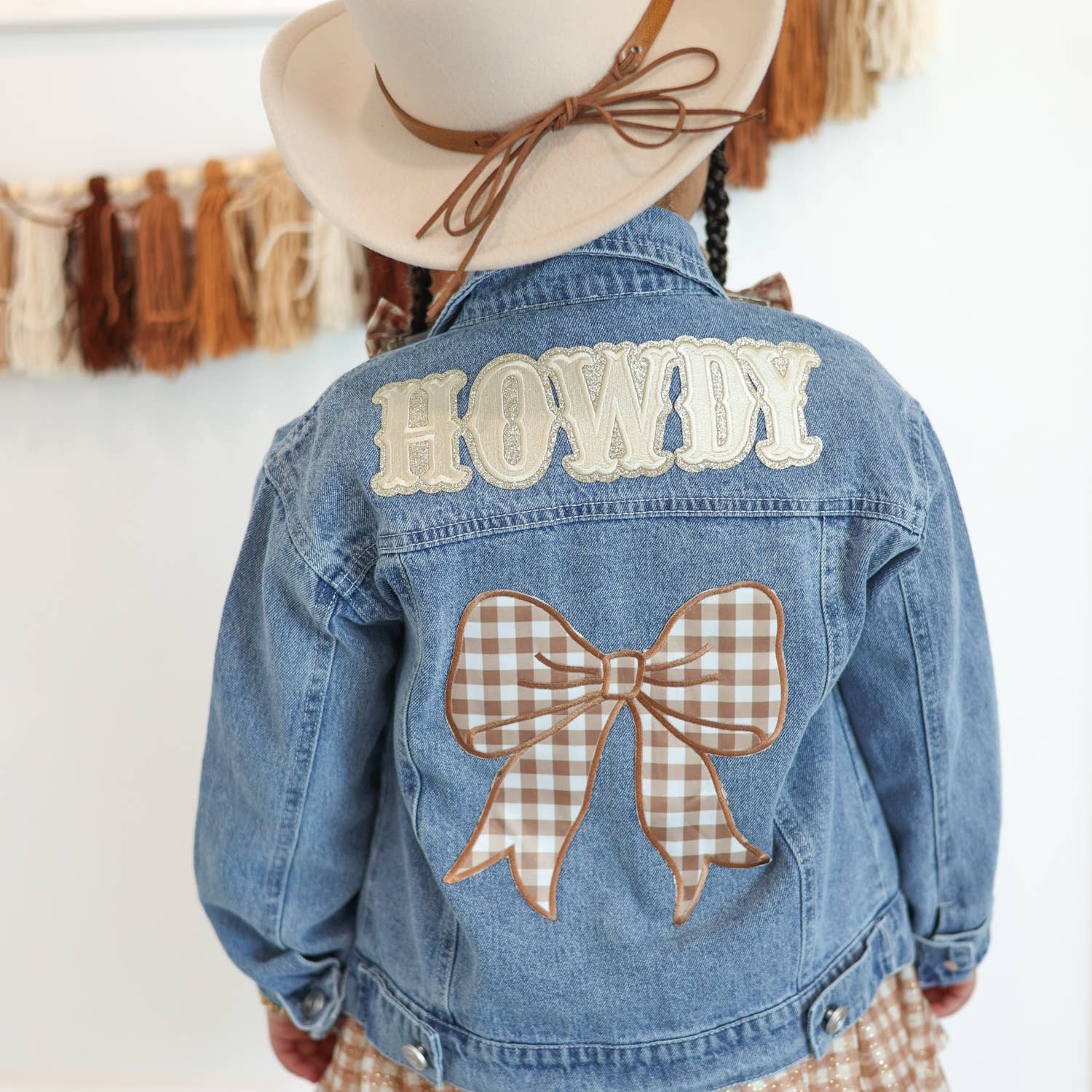 Denim jacket with 'HOWDY' and bow design, worn by a child.