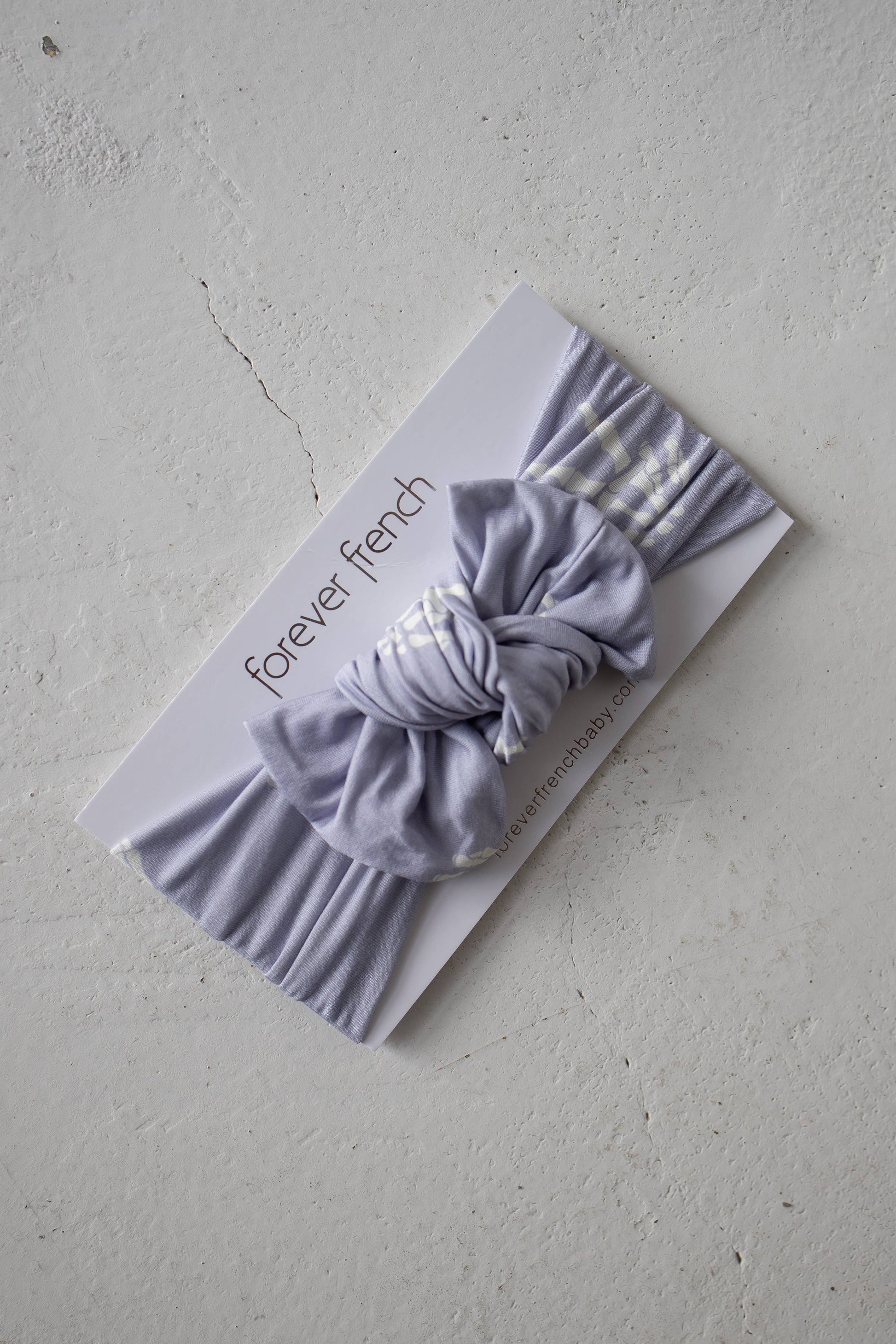 Lavender Enchanted Skelly bamboo head wrap with bow, flat lay on a textured stone background