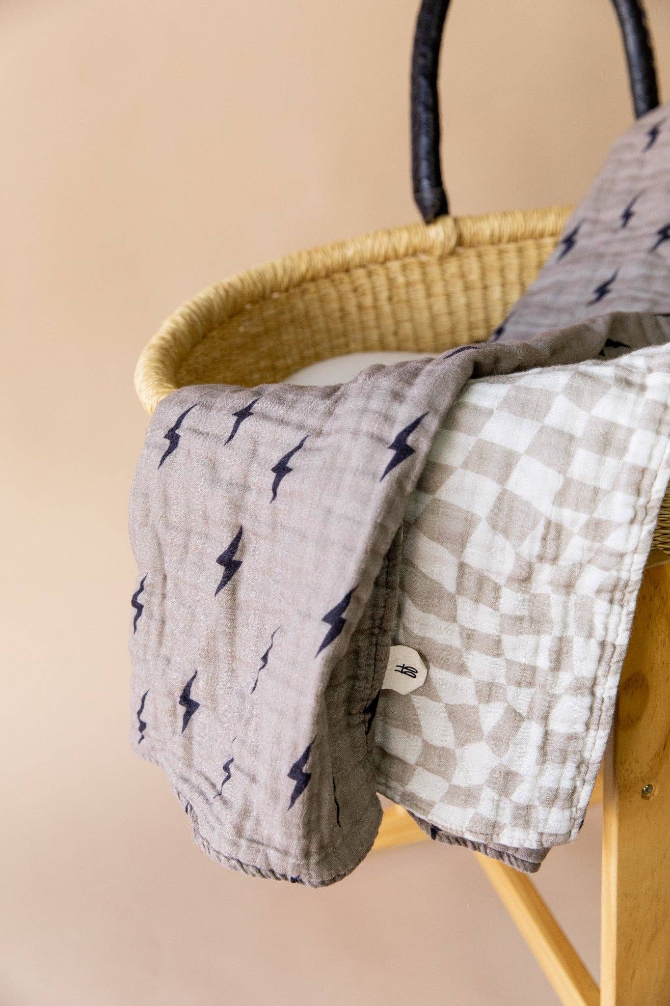 Lightning bolt print side of the muslin baby quilt draped over a yellow moses basket