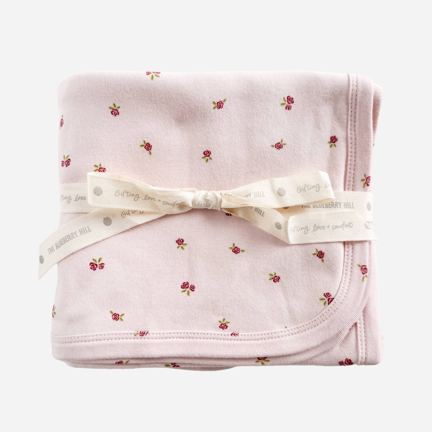 Folded pink blanket with floral pattern and white ribbon on a white background