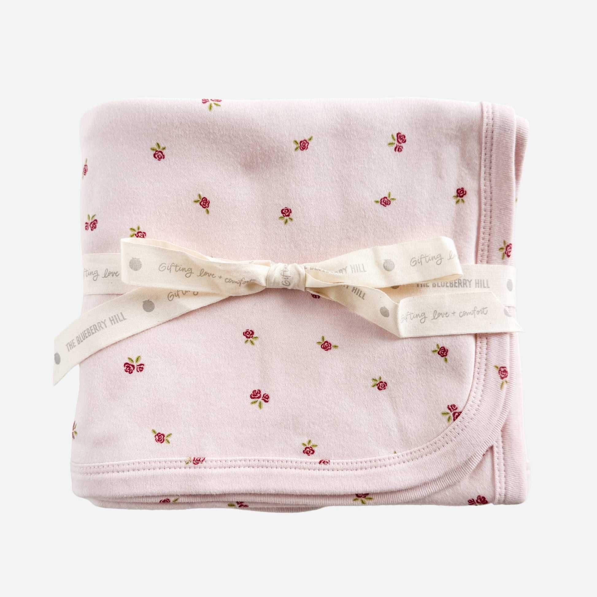 Folded pink blanket with floral pattern and white ribbon on a white background