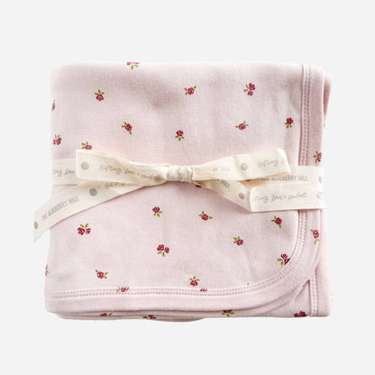 Folded pink blanket with floral pattern and white ribbon on a white background