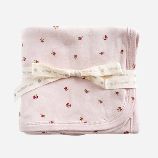 Folded pink blanket with floral pattern and white ribbon on a white background