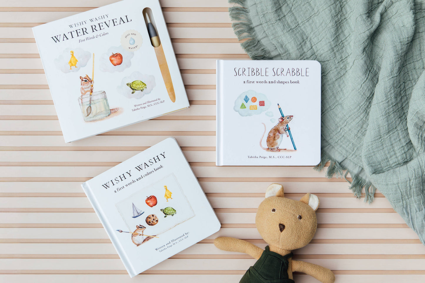 Three children's books on a striped surface with a plush toy and blanket.