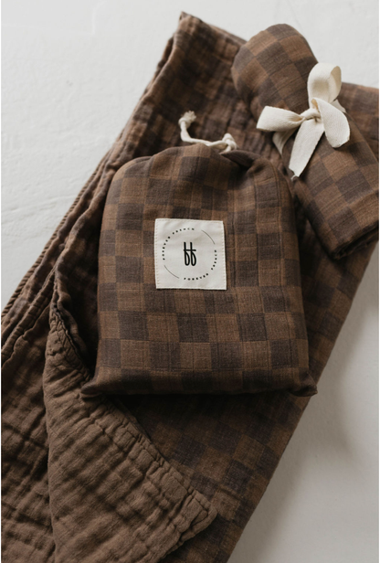 Folded faded brown checkerboard muslin baby quilt with a knotted lovey, showing the Forever French Baby tag