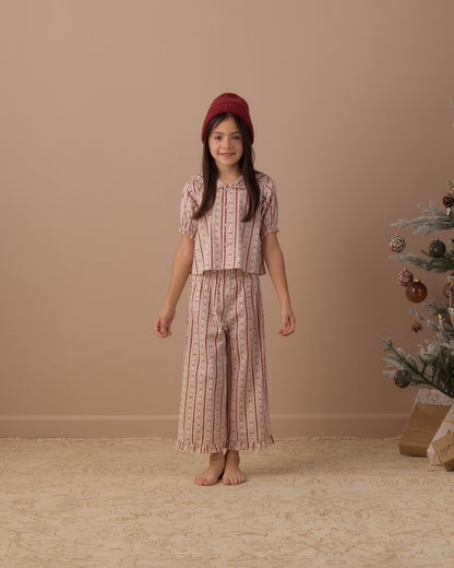 Girl in a red beanie wearing the Rylee + Cru ruffle pajamas in candy cane lane stripe, front view